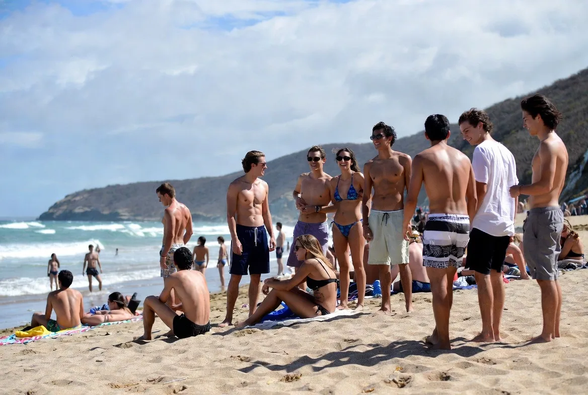 Group of young travelers in swimsuits socializing on Zipolite beach with Pacific surf and headland behind them