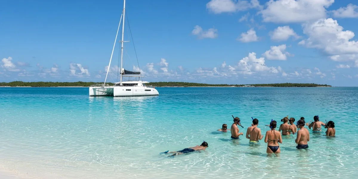 Snorkelers wading in shallow turquoise water beside a catamaran anchored off a white sand beach near Cancun