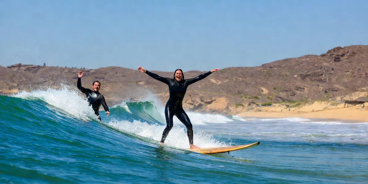 Beginner surfers riding small clean waves at Playa Cerritos near Todos Santos with desert hills behind the beach
