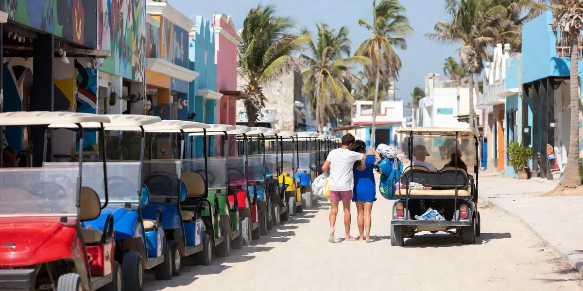 Row of rental golf carts parked on a sandy Holbox street with colorful facades behind