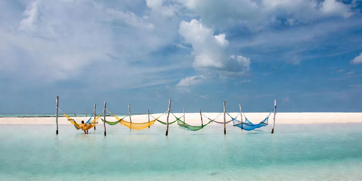 Hammocks strung in the shallow water off Isla Holbox with a long white sandbank behind