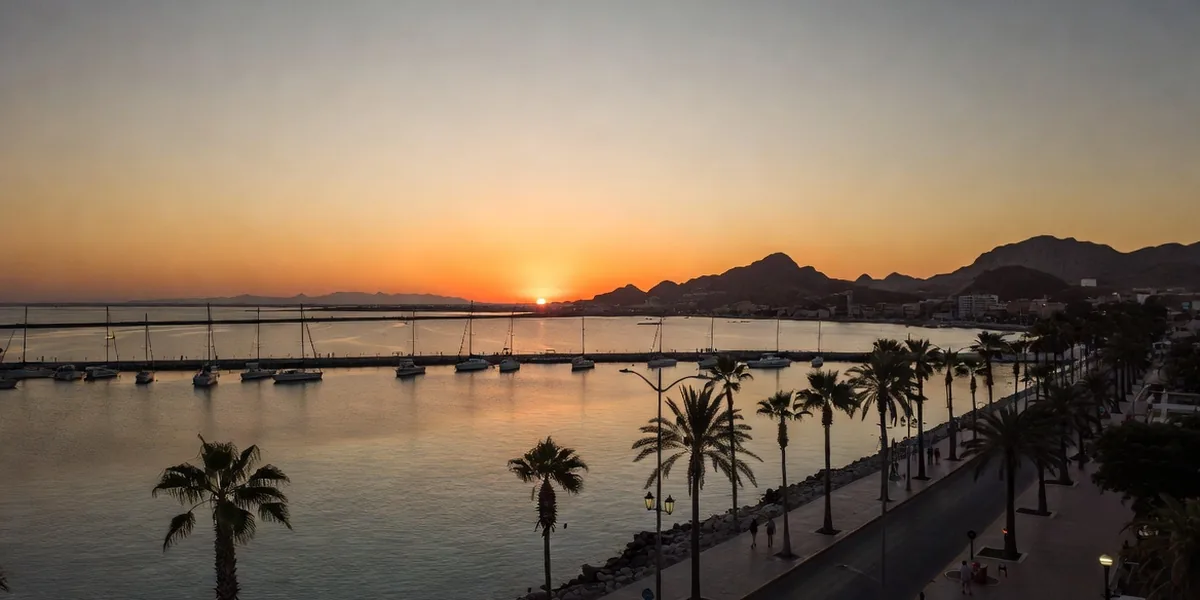 The La Paz malecón at sunset with palms, strollers and sailboats moored on the calm bay