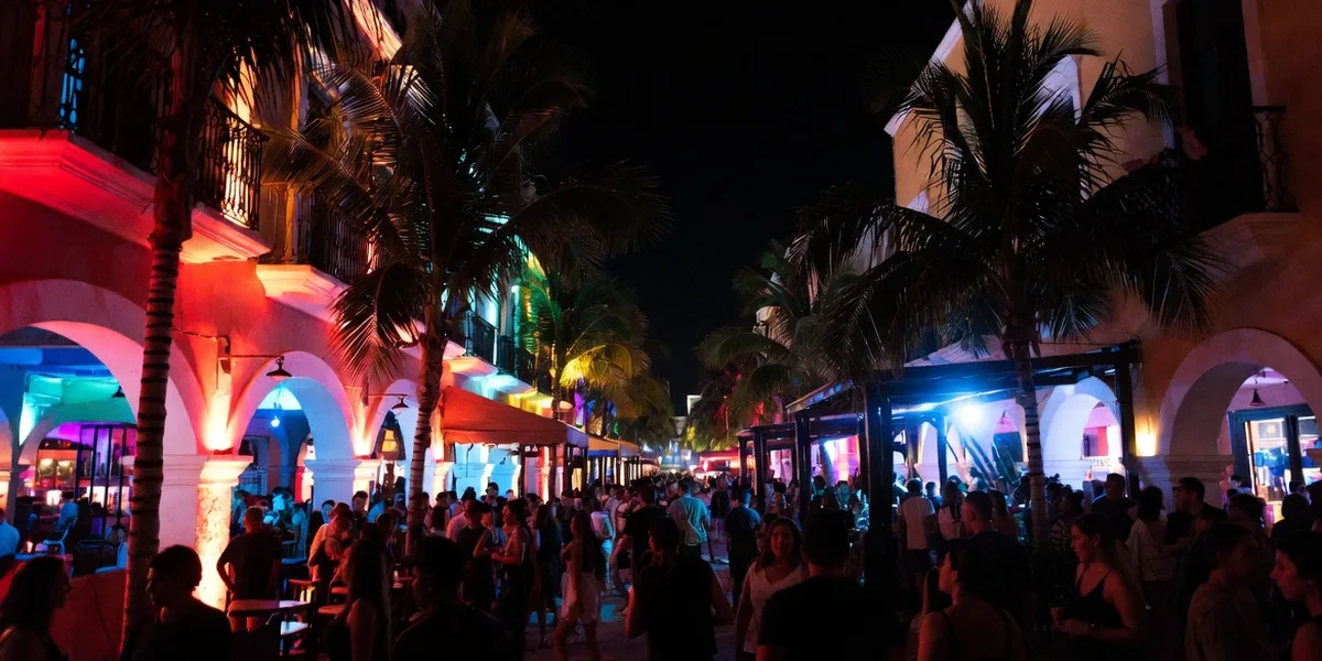 Crowds under neon palms on Playa del Carmen's 12th Street club strip at night