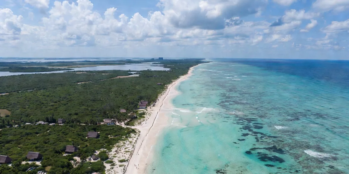 Aerial of the Riviera Maya coastline with reef bands, white beach and jungle stretching to the horizon