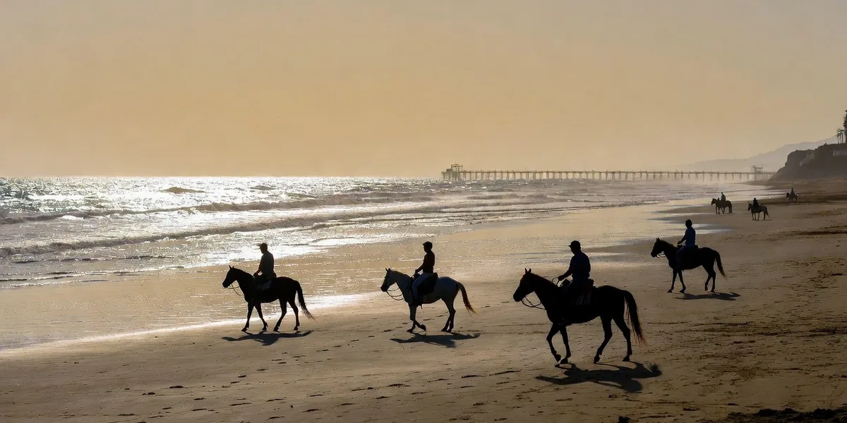 Wide Rosarito beach at golden hour with horseback riders on the sand and the pier in the distance