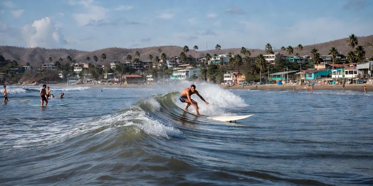 Longboarder riding a mellow right-hand wave at Sayulita's main break with the town behind