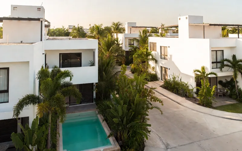 Modern white apartment buildings with a small pool surrounded by palms in Aldea Zama, Tulum